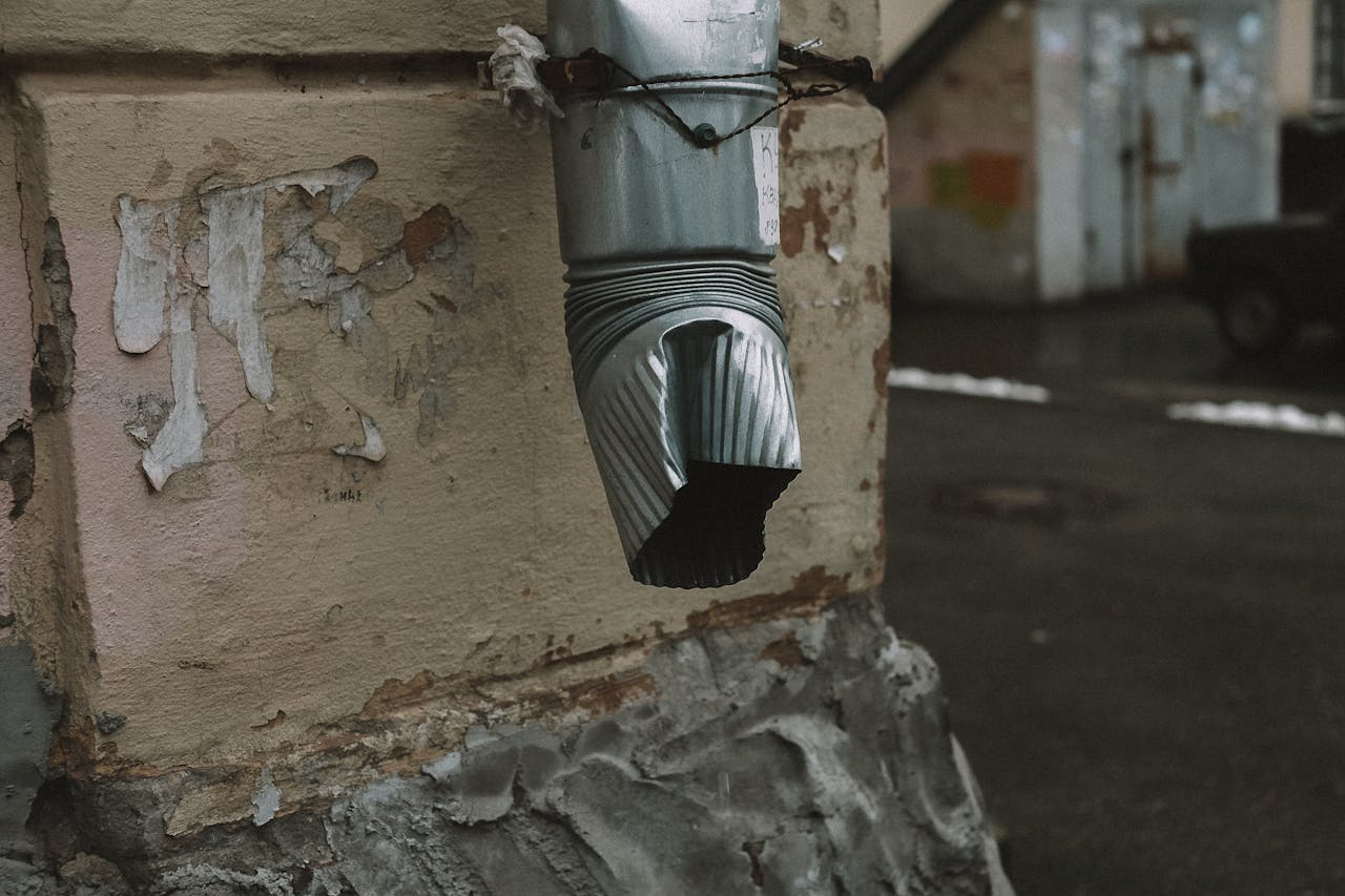 A metal drainage pipe with a rustic appearance on an aged wall with flaking paint.